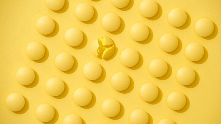 Bright yellow pills in a row on yellow background.